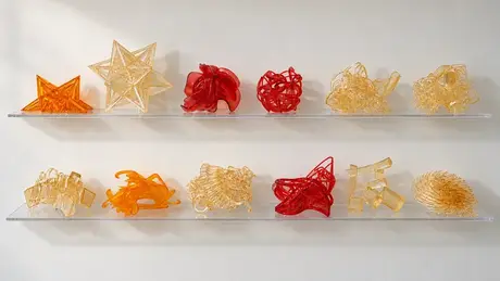 Printed sculpture studies on two shelves, stars and tangled forms in amber and red