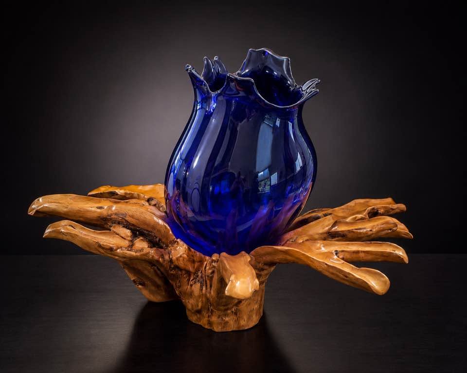 Deep blue blown glass vessel with a flared rim, set into a pale root-wood base
