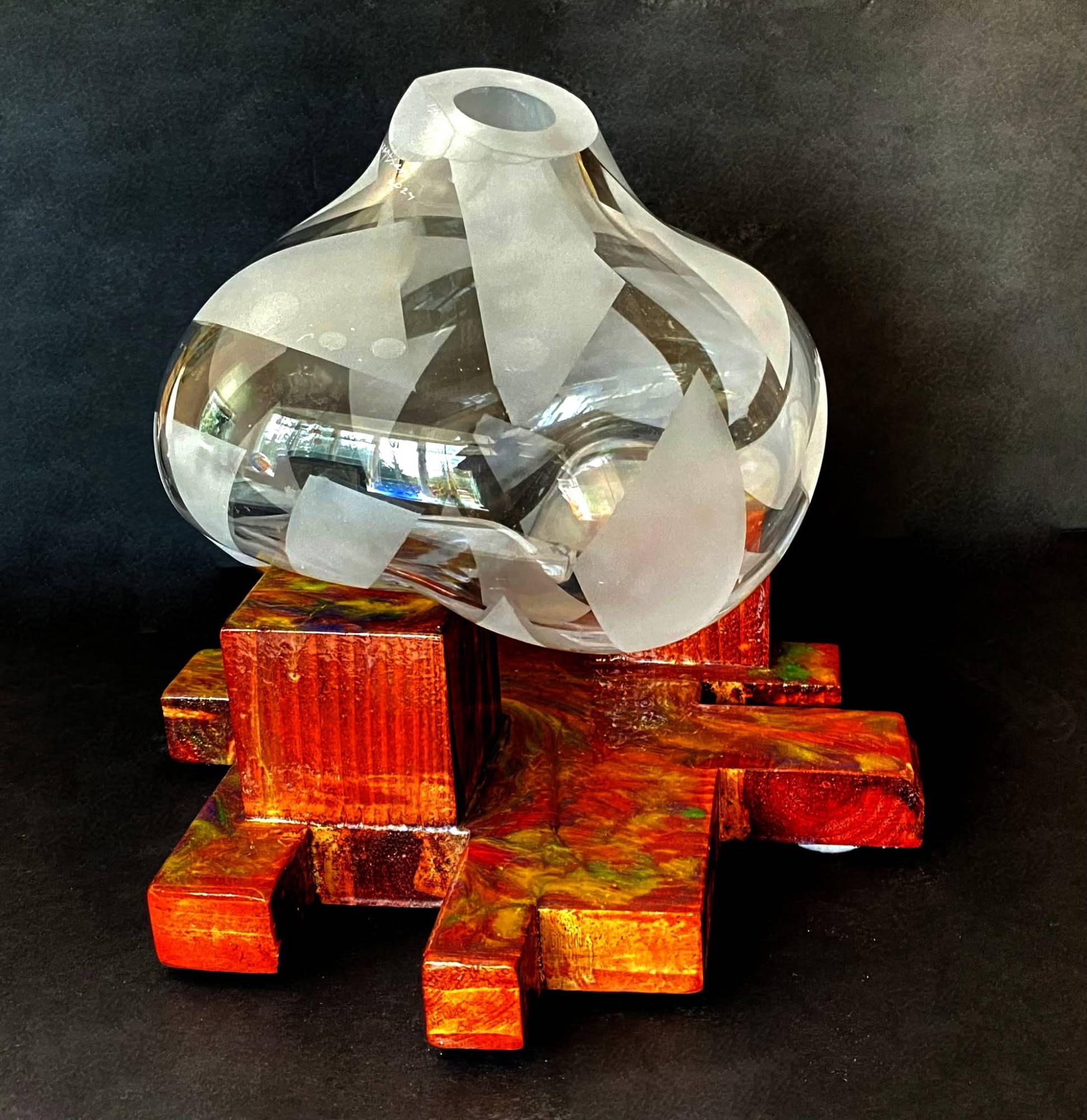 Frosted and clear blown glass vessel resting on an orange resin and wood base