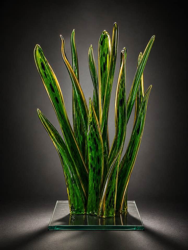 Tall green and gold glass blades with dark markings on a clear glass base