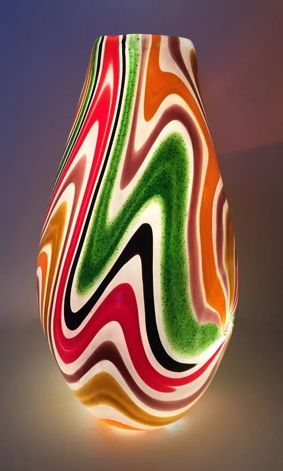 A tall blown glass vase in red, green, orange, black and white, the colours combed into deep zigzag waves running round the body