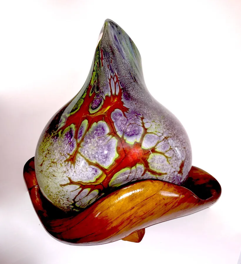 A blown glass vessel in white, violet and green, its surface broken into wide cells with red veins running between them, resting in a flared amber and red glass base