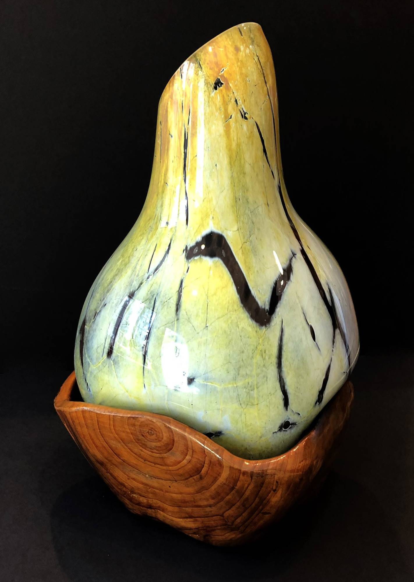 The Igal, a pale yellow and green crackled blown glass vessel with dark veining, seated in a carved wood bowl